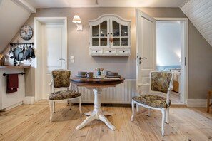 A dining area with a round table, two chairs, a cabinet with glass doors, and a clock on the wall.