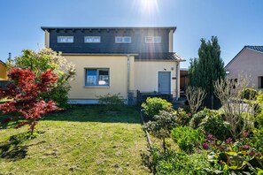 Una casa a due piani con un cortile anteriore, un piccolo giardino e un cielo sereno.