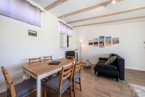 Zona pranzo con tavolo e sedie in legno, un divano nero e una TV su un mobile.
