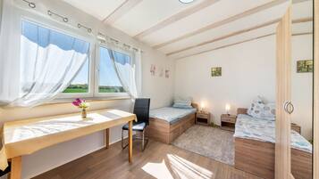 A bedroom with a wooden desk, a chair, a bed, a bedside table, and a window with curtains.