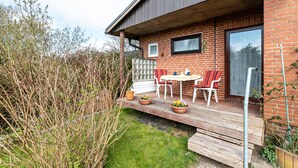 Een modern huis met een bakstenen gevel, een houten terras met tuinmeubels, en een groot raam.