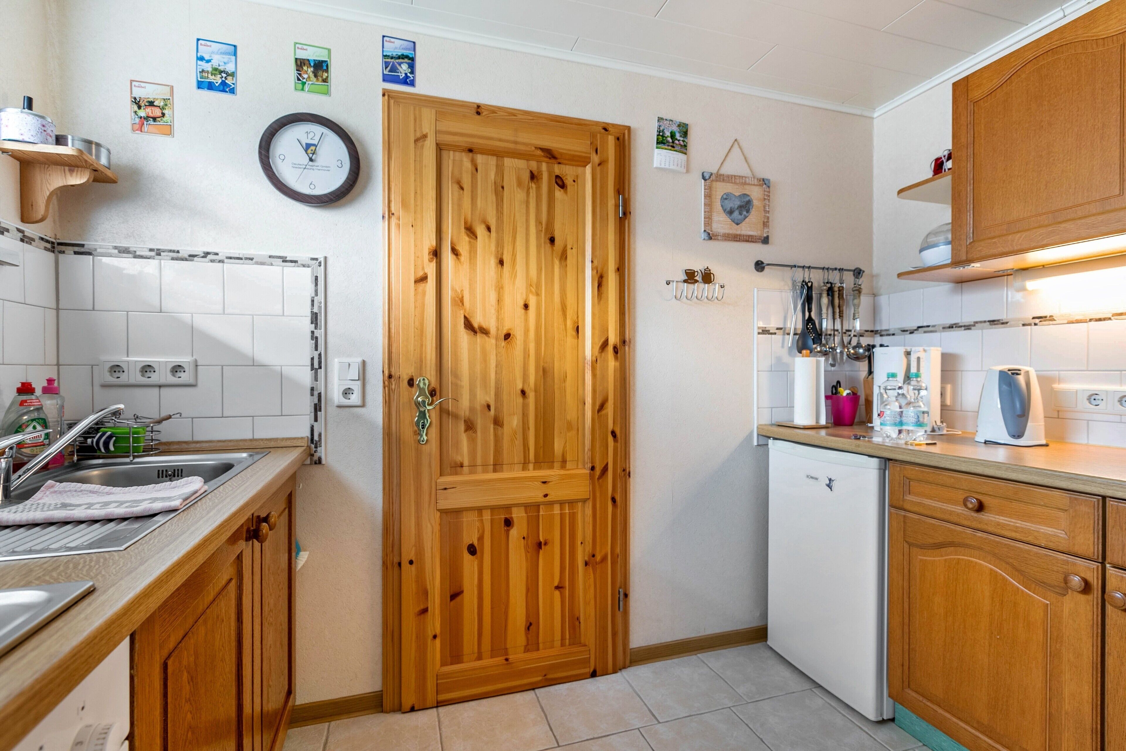 Une cuisine avec des meubles en bois, un lave-vaisselle blanc et une horloge au mur.