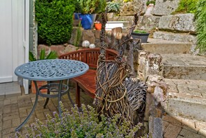 Eine Terrasse mit einem Metalltisch und -stühlen, einer Steinmauer und einer dekorativen Rankhilfe für Pflanzen.