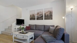 A modern living room with a grey sofa, white coffee table, and a flat-screen TV on a white stand. - Apartment 'Bianca' with Private Terrace, Private Garden and Wi-Fi (Offenburg)