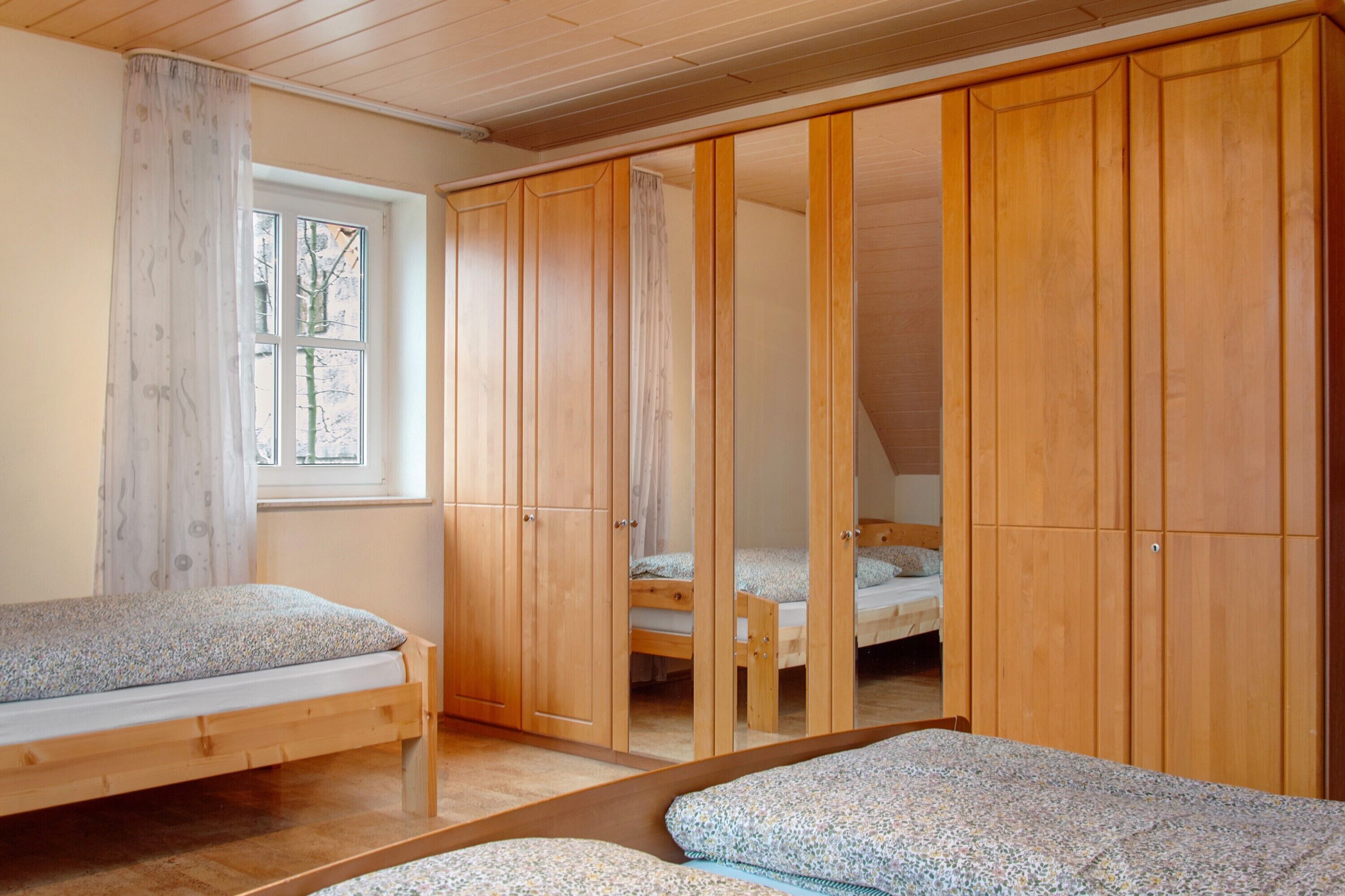 A bedroom with two single beds, wooden wardrobes, a window, and a view of trees outside.