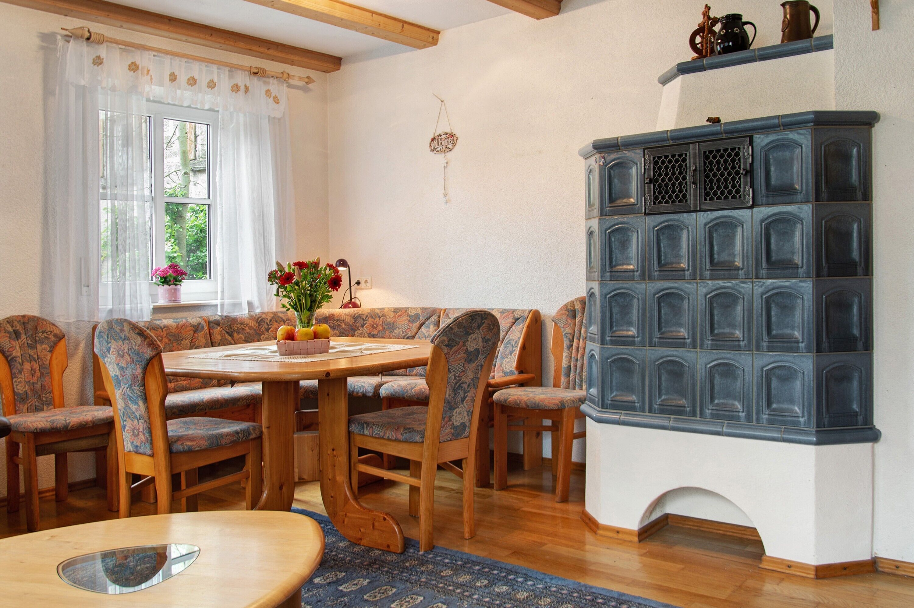 Een eetgedeelte met een houten tafel en stoelen, een raam met gordijnen en een blauwe kast met meerdere vakken.