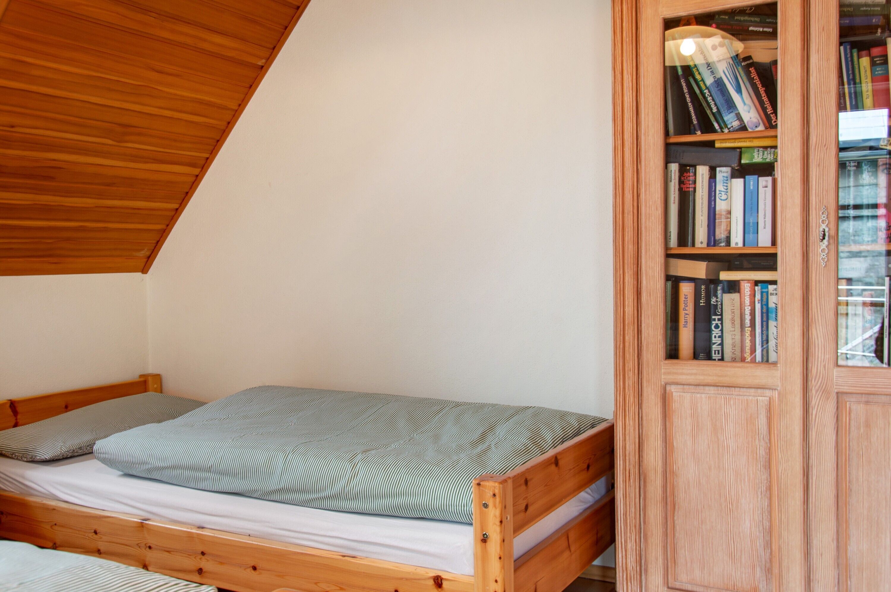 A wooden bed with a mattress and pillows, a wooden bookshelf with books, and a sloped ceiling.