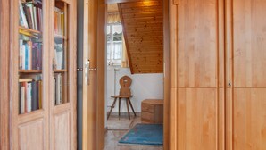 Un corridoio in legno con una libreria, una piccola sedia di legno, un termosifone e un tappeto blu.