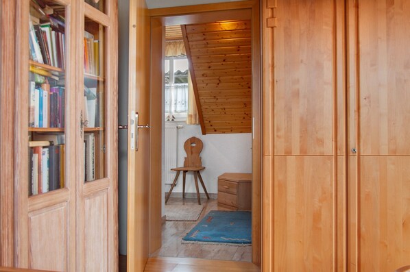 Un pasillo de madera con una estantería, una pequeña silla de madera, un radiador y una alfombra azul.
