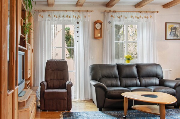 Un salon avec un canapé en cuir marron, une table basse en bois, un fauteuil marron et un téléviseur posé sur un meuble en bois.