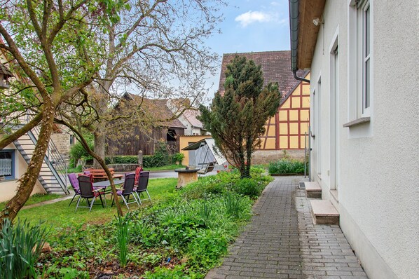 A courtyard with a table and chairs, a tree, and a building with a sloped roof.