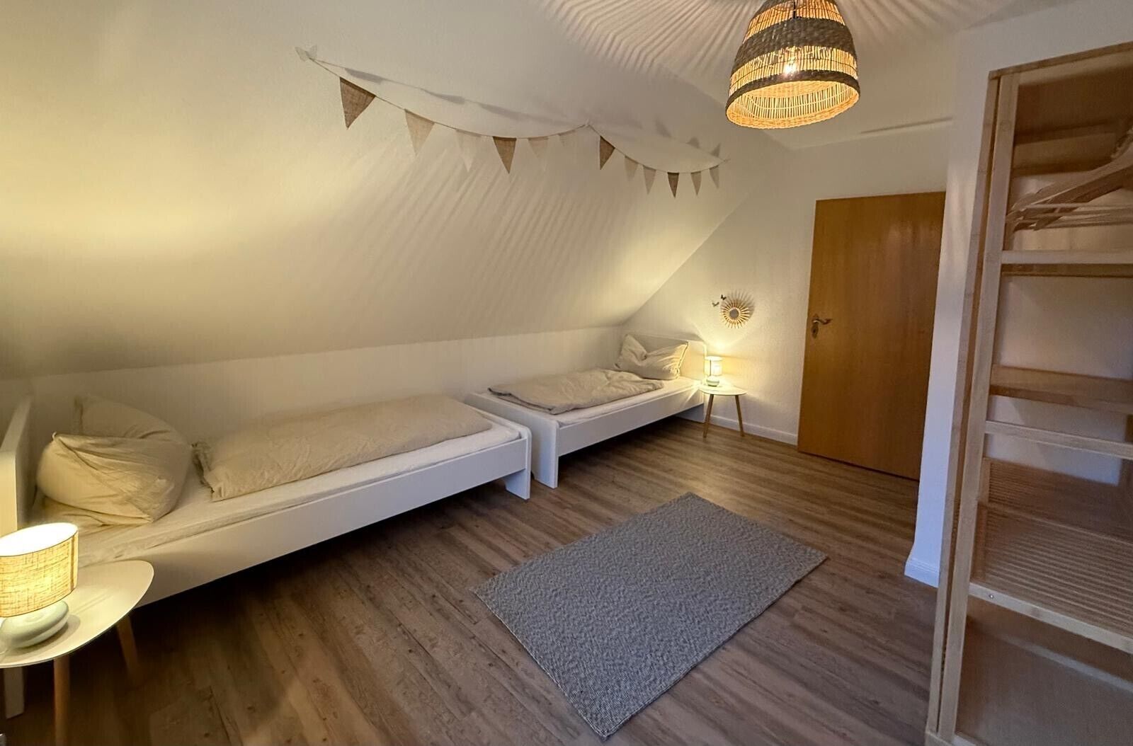 A cozy attic bedroom with a loft bed, a small bedside table with a lamp, and a wooden door.