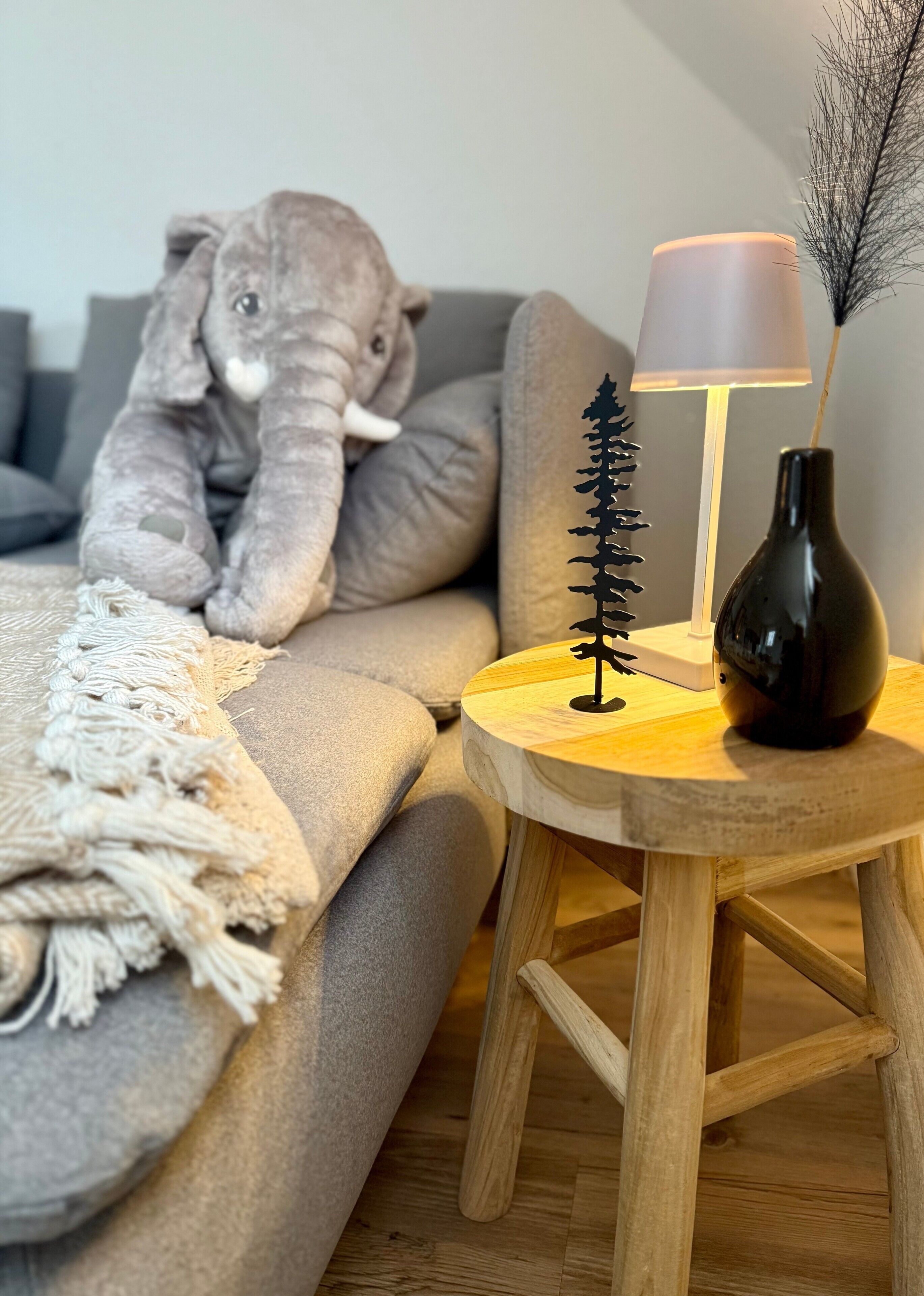 A cozy room with a sofa, a lamp, a small tree decoration, and a stuffed elephant toy.