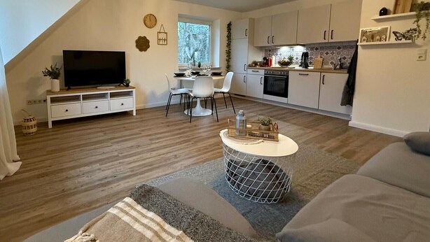 A modern living room with a TV, sofa, and dining area. - Apartment 'Hygge' with Private Terrace, Private Garden and Wi-Fi (Hennstedt)