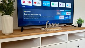 A television on a wooden TV stand with a white cabinet below. - Apartment 'Hygge' with Private Terrace, Private Garden and Wi-Fi (Hennstedt)