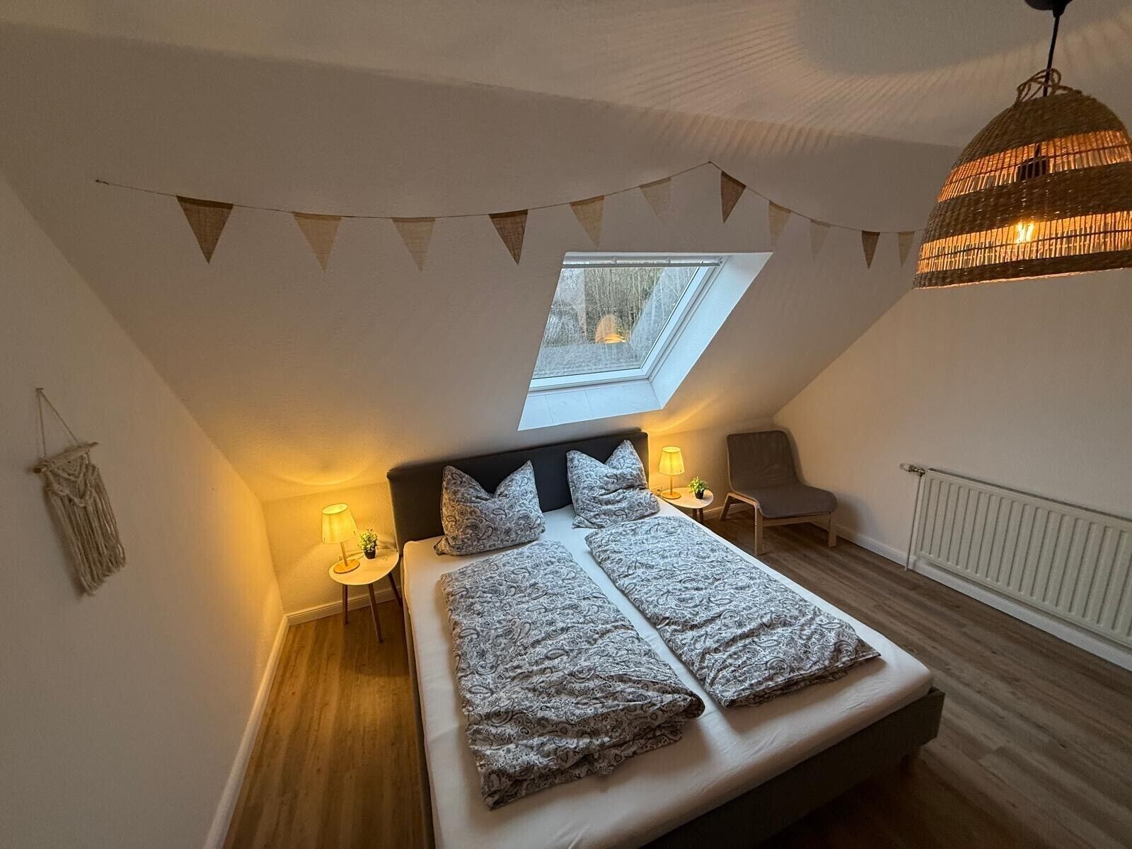 Une chambre avec un puits de lumière, un lit avec une literie à motifs, une chaise, une lampe et un luminaire suspendu.