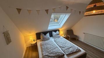 Une chambre avec un puits de lumière, un lit avec une literie à motifs, une chaise, une lampe et un luminaire suspendu.