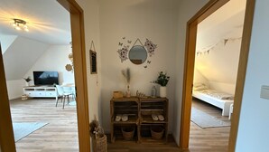 A room with a wooden floor, a TV, a desk, a chair, a bed, and a shelf with shoes. - Apartment 'Hygge' with Private Terrace, Private Garden and Wi-Fi (Hennstedt)