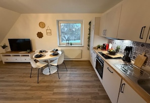 A modern kitchen with a dining area, a TV, and a window with a view of trees. - Apartment 'Hygge' with Private Terrace, Private Garden and Wi-Fi (Hennstedt)