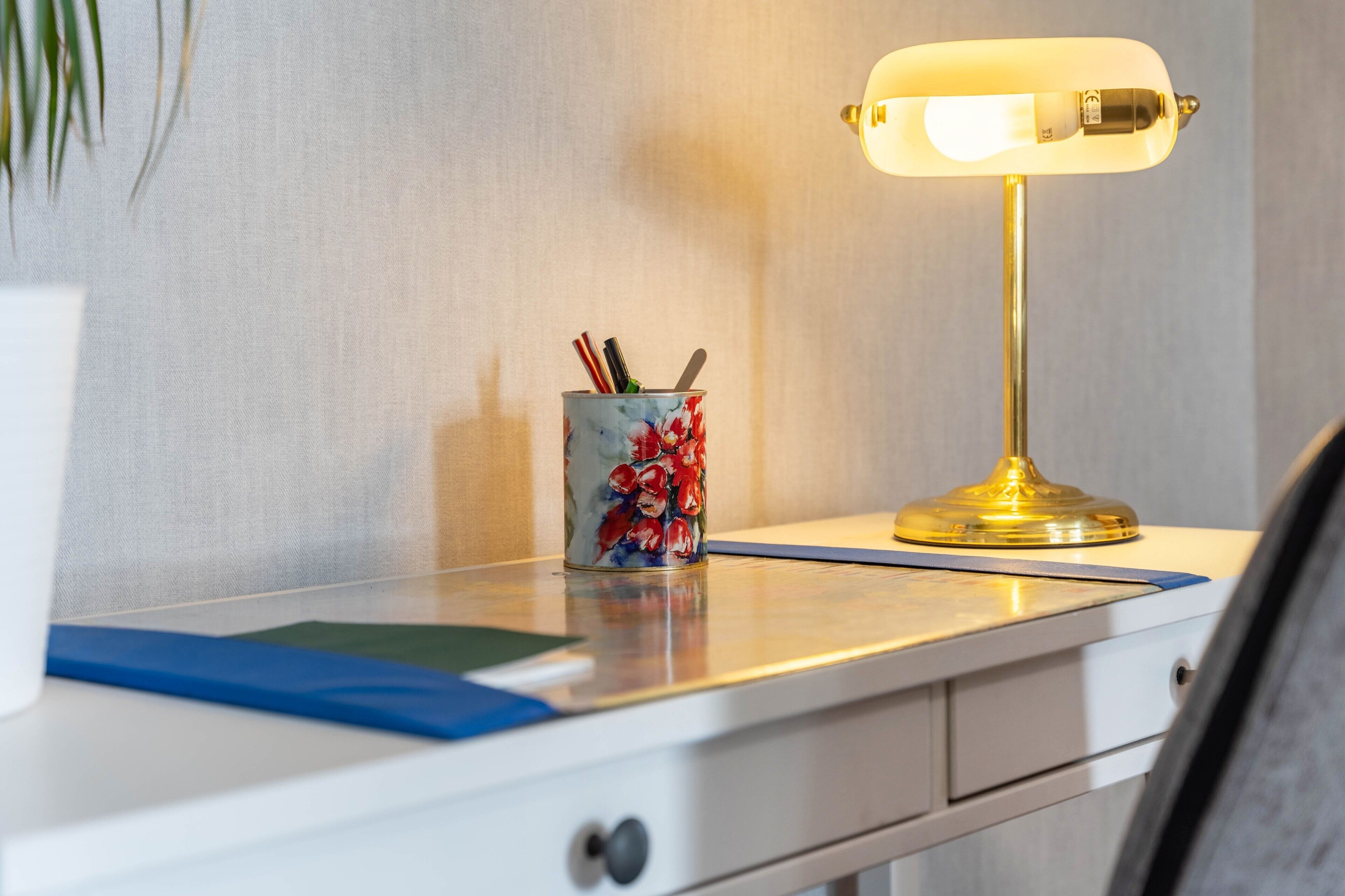 Een bureau met een lamp, een beker met pennen en een plant.