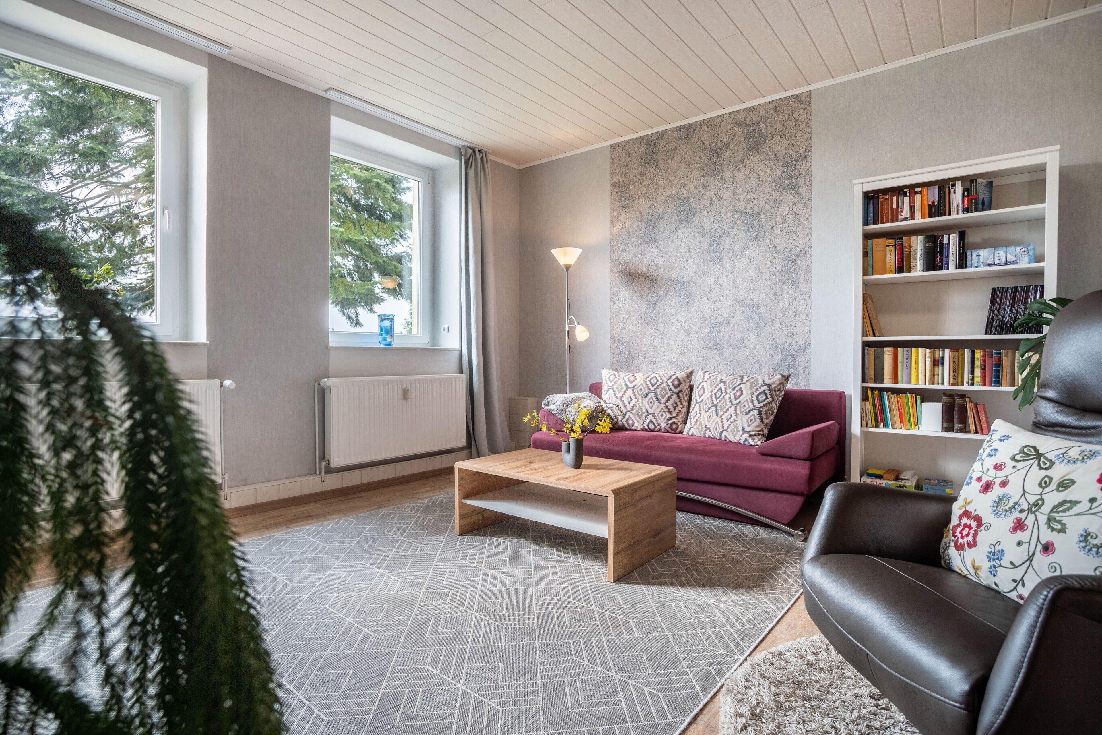 Ein modernes Wohnzimmer mit einer Couch, einem Couchtisch, einem Bücherregal und einem großen Fenster.