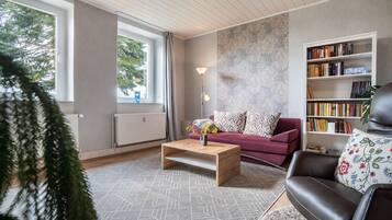 Ein modernes Wohnzimmer mit einer Couch, einem Couchtisch, einem Bücherregal und einem großen Fenster.