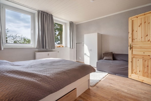A bedroom with a bed, a wardrobe, a radiator, a window with curtains, and a door.