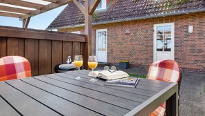 An outdoor wooden table with two glasses of orange juice, a book, and a pair of sunglasses.