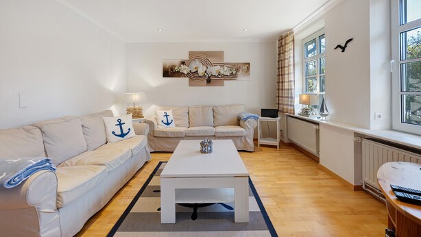 A living room with a white sofa, a coffee table, a painting, and a window with curtains.