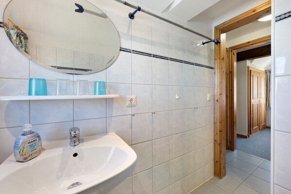 Une salle de bain avec un lavabo blanc, un miroir, un espace douche et une porte en bois.