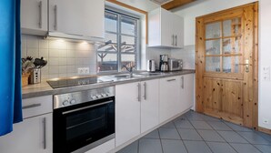 Une cuisine moderne avec des armoires blanches, des appareils en acier inoxydable, une porte en bois et une fenêtre.