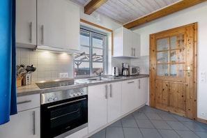 A modern kitchen with white cabinets, stainless steel appliances, a wooden door, and a window.