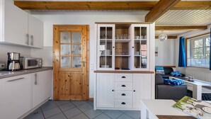 Une cuisine compacte avec des meubles blancs, une porte en bois et un meuble intégré doté de portes en verre.