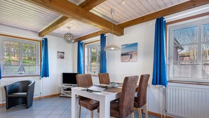 Un espace repas comprenant une table, des chaises, un téléviseur et une fenêtre avec des rideaux.