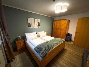 A bedroom with a wooden bed, a wardrobe, a nightstand, and a wall-mounted light fixture.