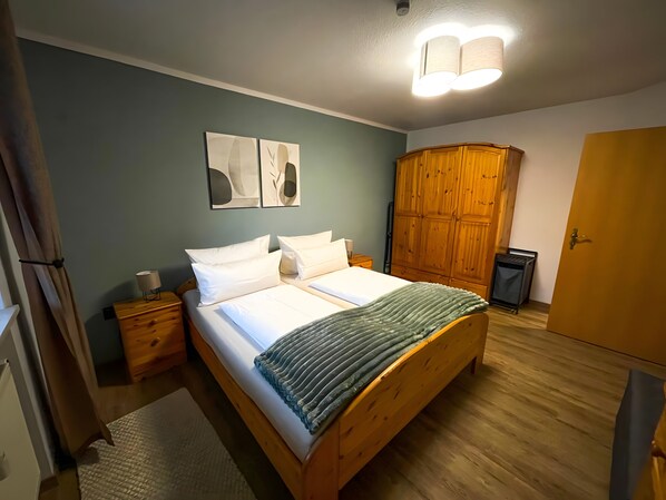 A bedroom with a wooden bed, a wardrobe, a nightstand, and a wall-mounted light fixture.