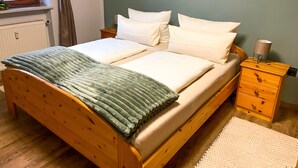 A double bed with a green blanket, a wooden nightstand with a lamp, and a wall with abstract art. - Apartment 'Bergliebe' with Mountain View, Balcony & WiFi (Weißbach an der Alpenstraße)