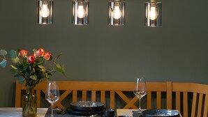 A dining area with a table set for two, a vase with flowers, and a wall-mounted painting of cows. - Apartment 'Bergliebe' with Mountain View, Balcony & WiFi (Weißbach an der Alpenstraße)