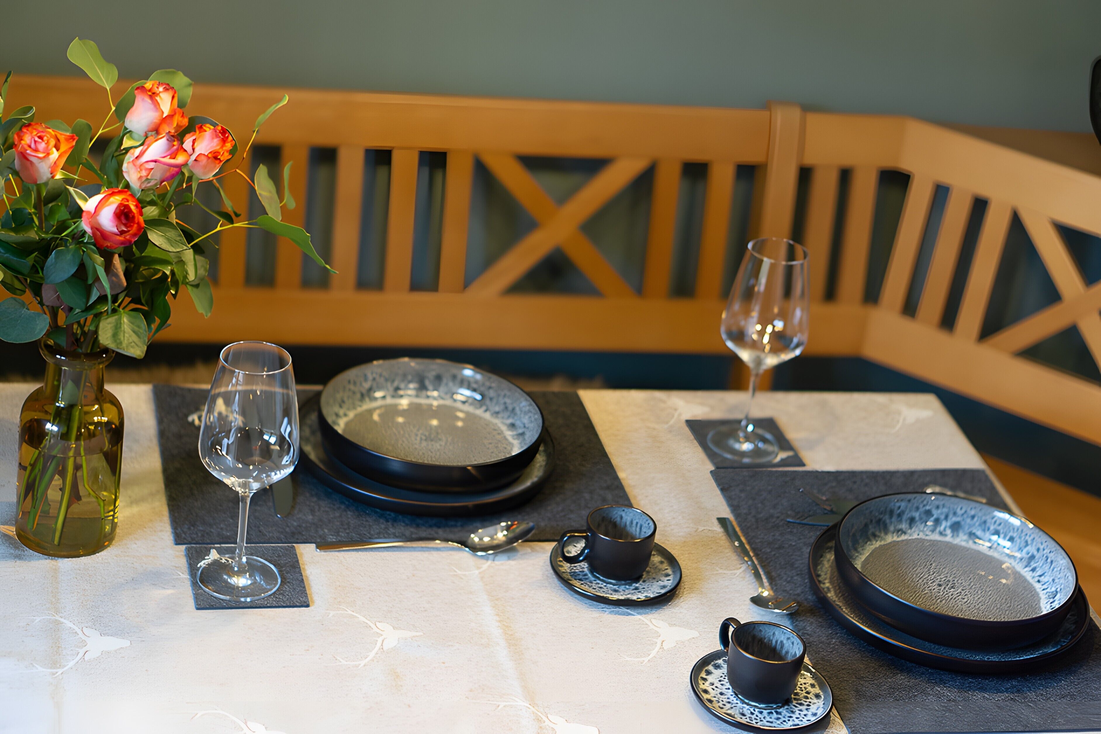 A dining table set with plates, glasses, and a vase of flowers.
