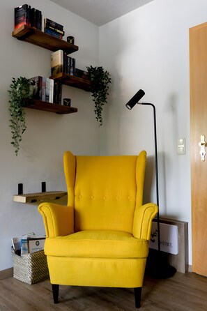 A yellow armchair, a black floor lamp, and wooden shelves with books and plants.