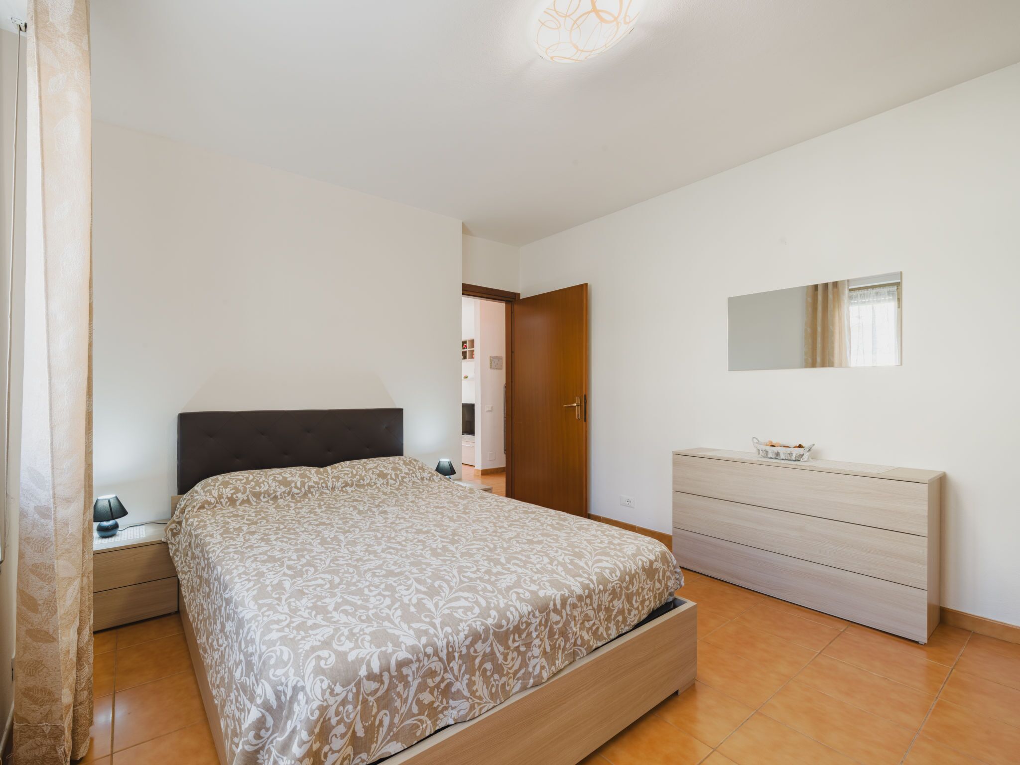 A bedroom with a bed, bedside table, dresser, and a mirror.