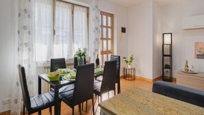 Un comedor con una mesa dispuesta para cuatro personas, sillas, un jarrón con flores y una planta en maceta sobre una mesita.