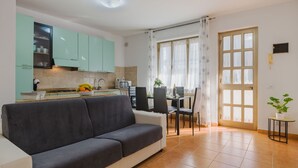 Una cocina moderna con armarios color turquesa, un comedor con mesa y sillas, y un sofá gris.