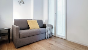 A modern living room with a grey sofa, a yellow pillow, a small side table, and a large window with a view. - Suite JOIVY Porta Torre 76 (Como)