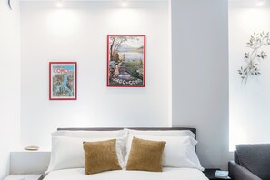 A modern hotel room with a bed, pillows, a nightstand, and two framed pictures on the wall.