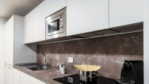 A modern kitchen with white cabinets, a built-in microwave, a black induction cooktop, and a coffee machine. - Suite JOIVY Porta Torre 76 (Como)