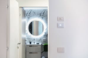 A bathroom with a marble wall, a round mirror with underglow lighting, a sink, and a towel rack.