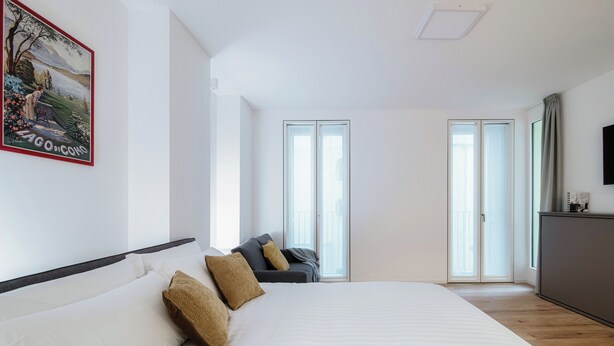 A spacious bedroom with a large bed, a sofa, and a TV. - Suite JOIVY Porta Torre 76 (Como)