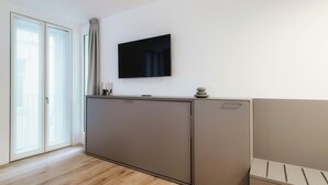 A modern room with a large cabinet, a flat-screen TV mounted on the wall, and a sliding glass door leading to an outdoor area. - Suite JOIVY Porta Torre 76 (Como)