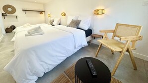 Une chambre d’hôtel moderne avec un grand lit, une chaise en bois, une petite table et une télécommande posée sur la table.